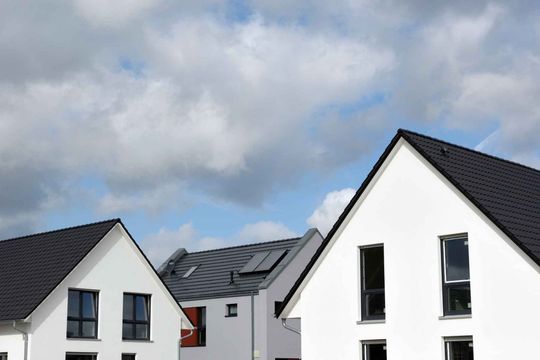 A row of white houses with black roofs against a cloudy sky