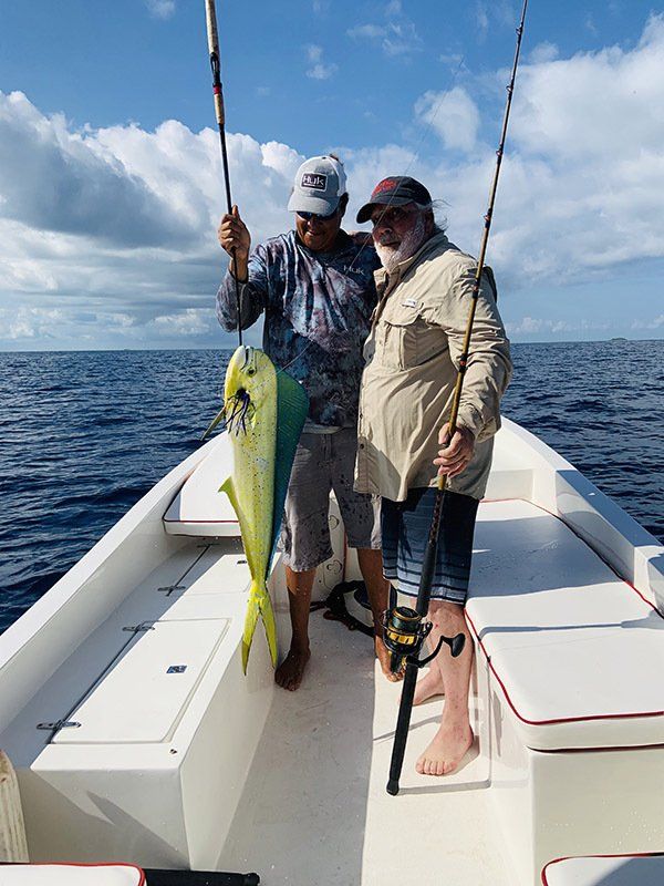Two men are standing on a boat holding fishing rods and a fish.