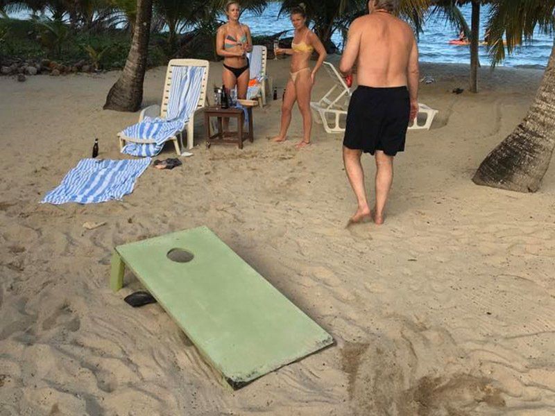 A man and two women are playing cornhole on the beach.