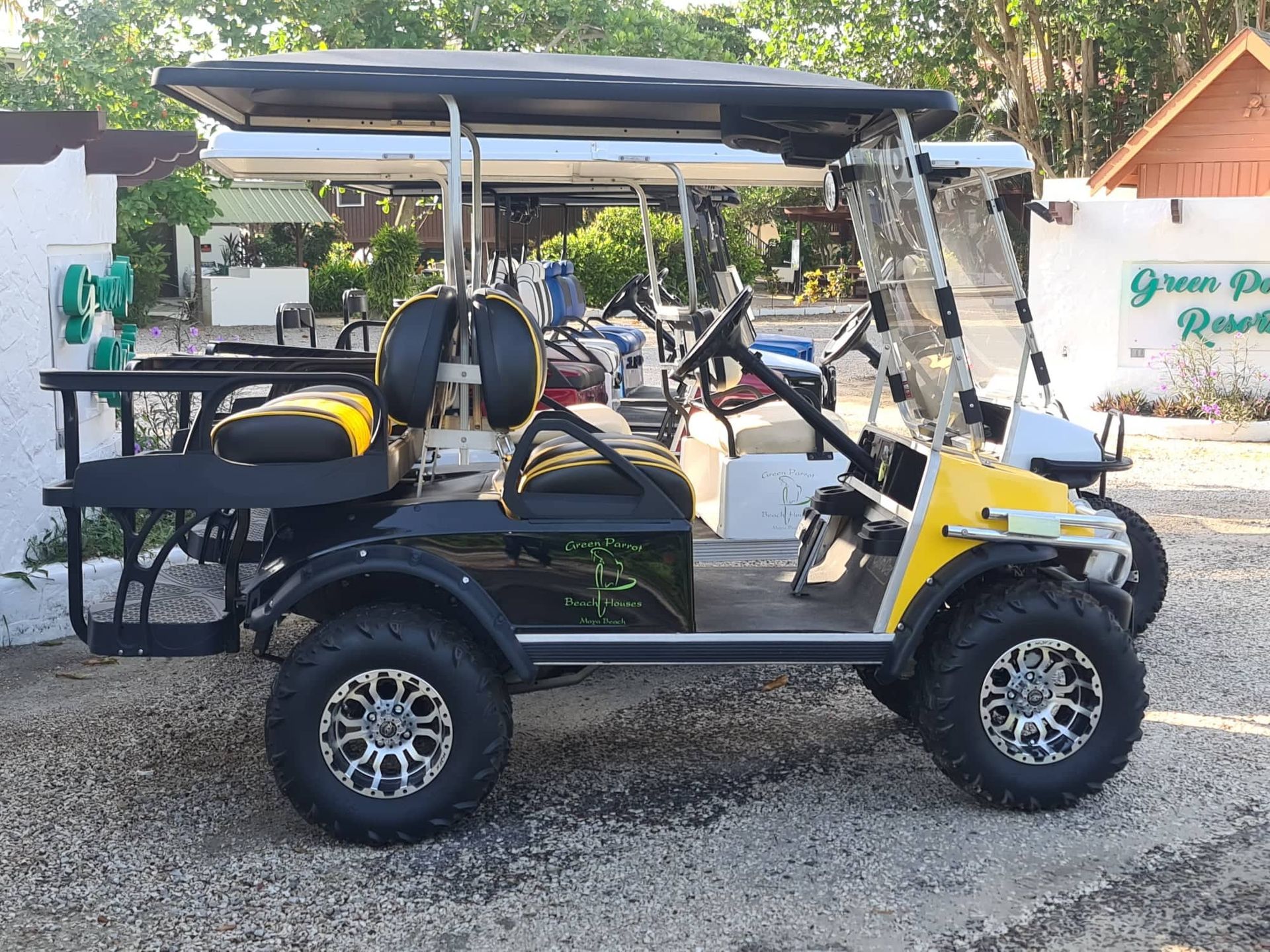 A yellow and black golf cart is parked in a gravel lot.