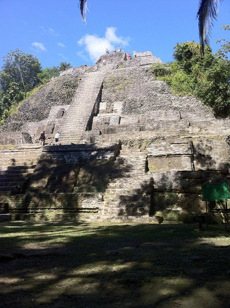 A large stone structure with stairs leading up to it is surrounded by trees and grass.
