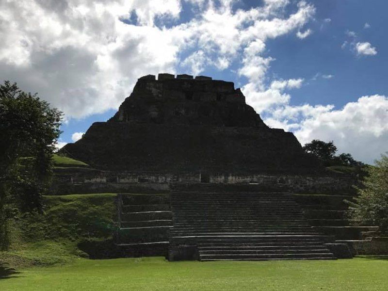 A large stone pyramid is surrounded by grass and trees.