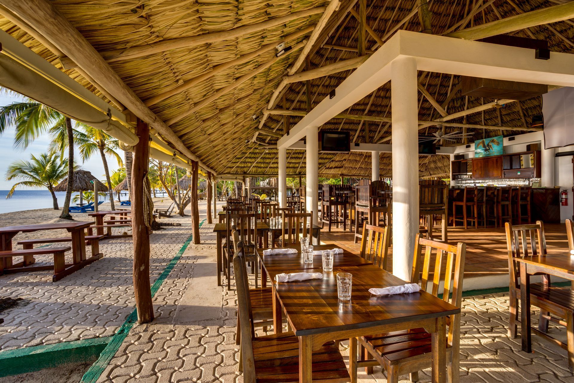 A restaurant with tables and chairs under a thatched roof.