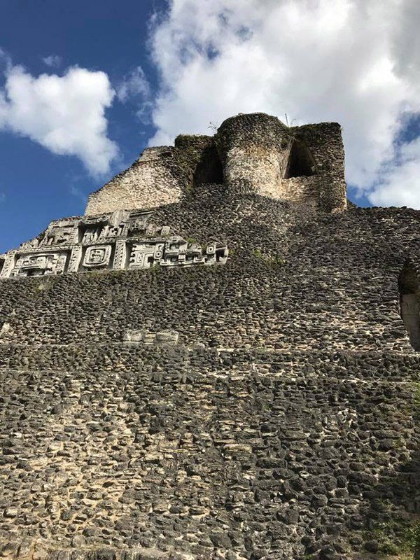 A large stone pyramid with a blue sky and clouds in the background.