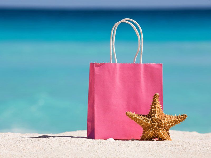 A pink shopping bag and a starfish are on the beach.