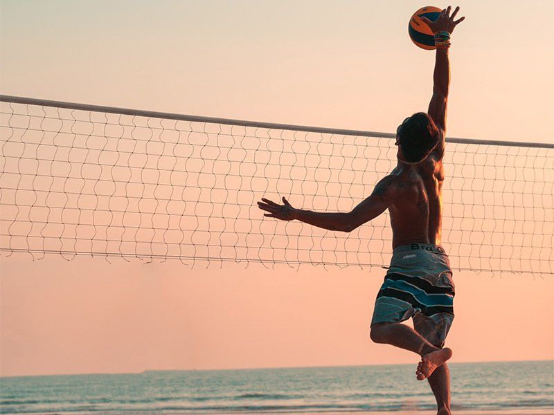 A man is jumping in the air to catch a volleyball on a beach.