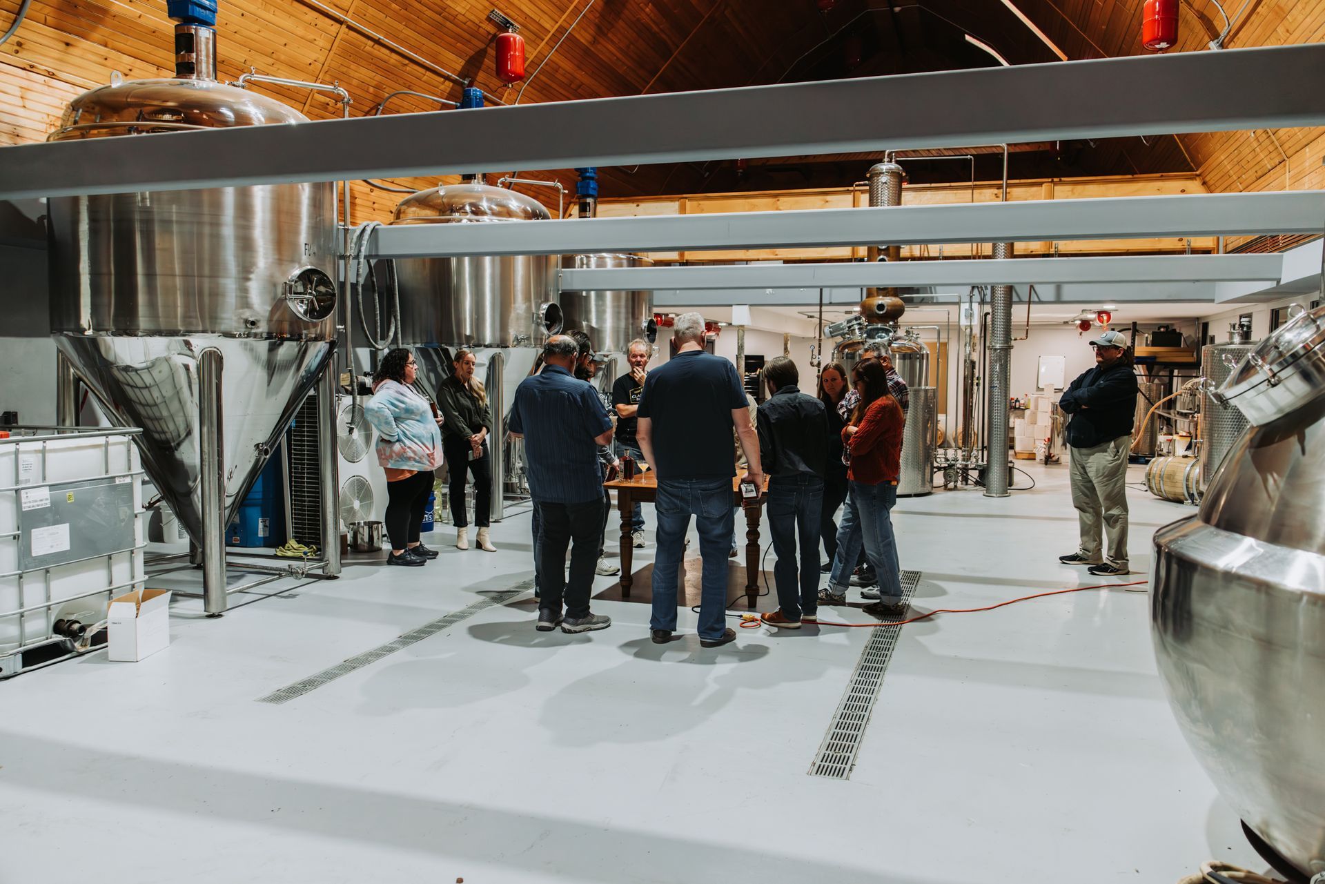 People gathered in a brewery, viewing equipment. Stainless steel tanks, and white floors are visible.