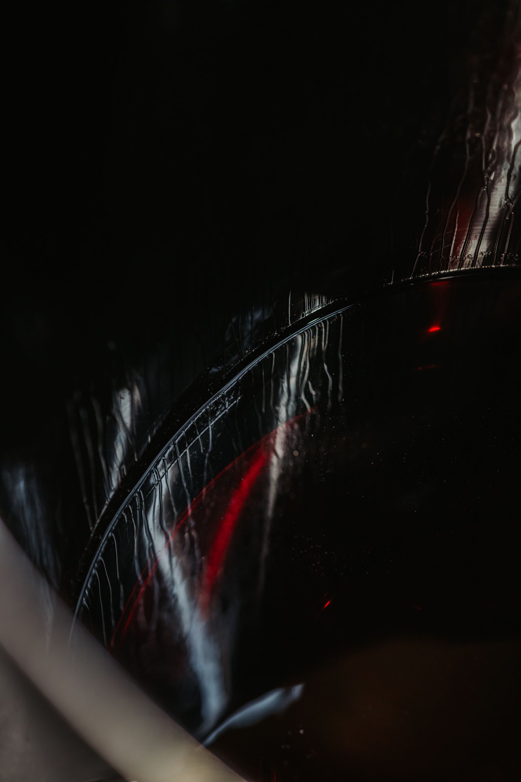 Black shiny surface with a curved seam, streaks of white, red glows, and a blurred white diagonal.