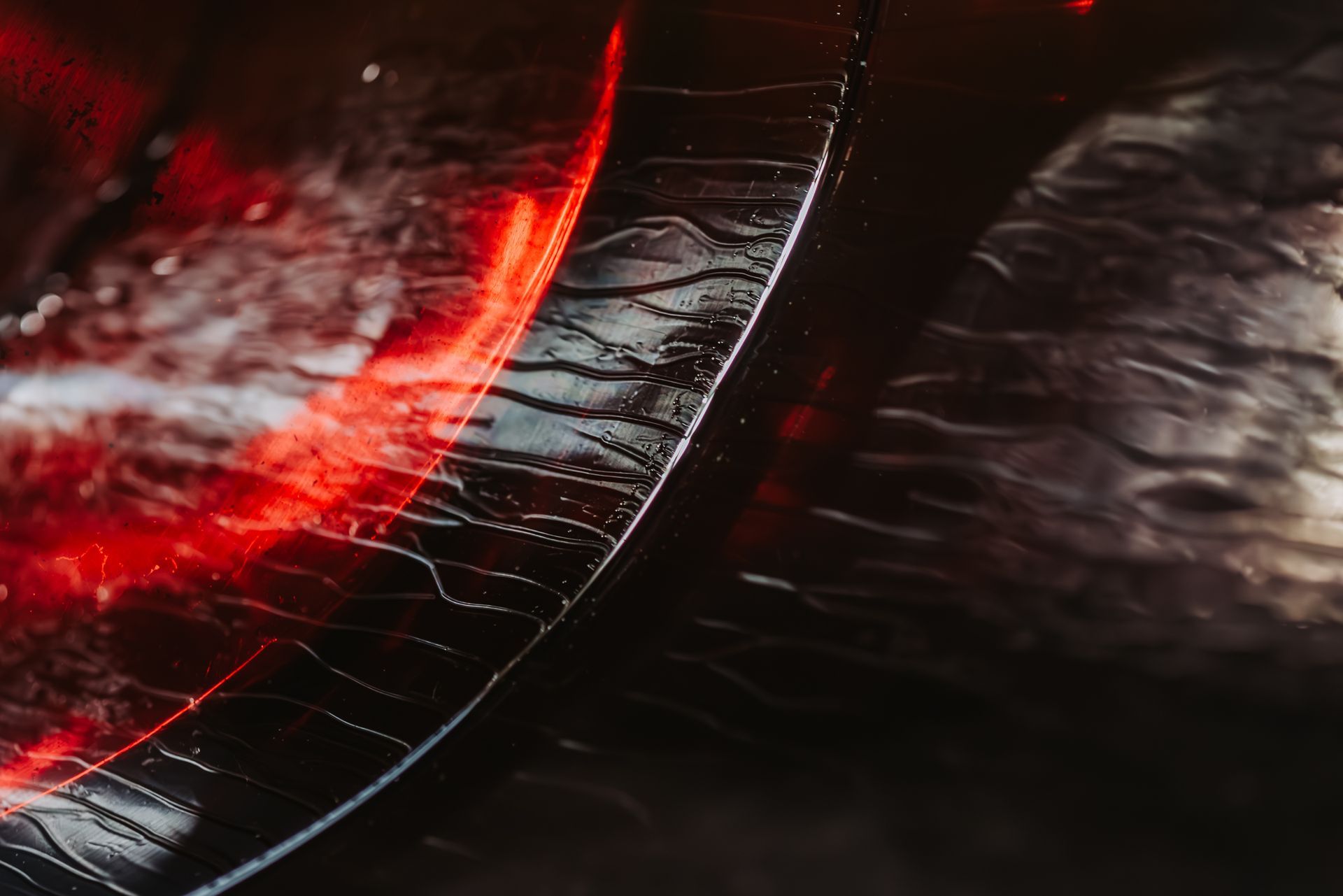 Black surface with wavy streaks, illuminated by red and white light, creating a reflective pattern.