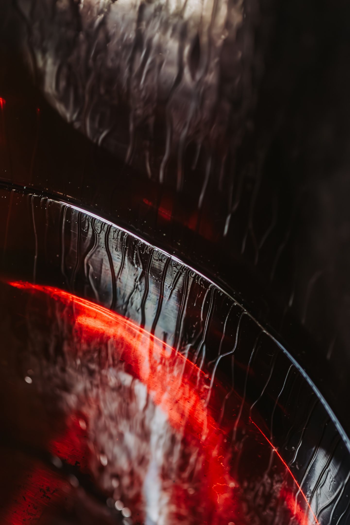 Abstract close-up, curved glass reflecting red light, textured surface, dark background.