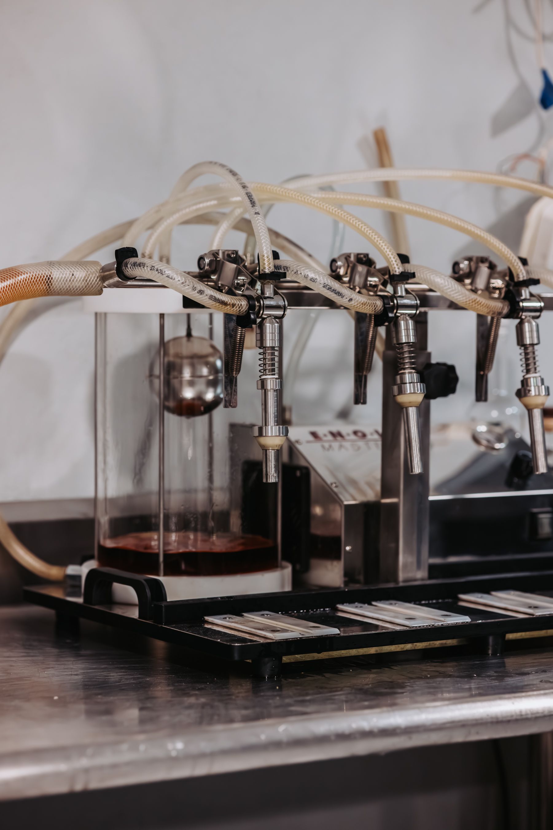 Stainless steel wine dispenser with multiple spouts and clear tubing, holding red liquid.