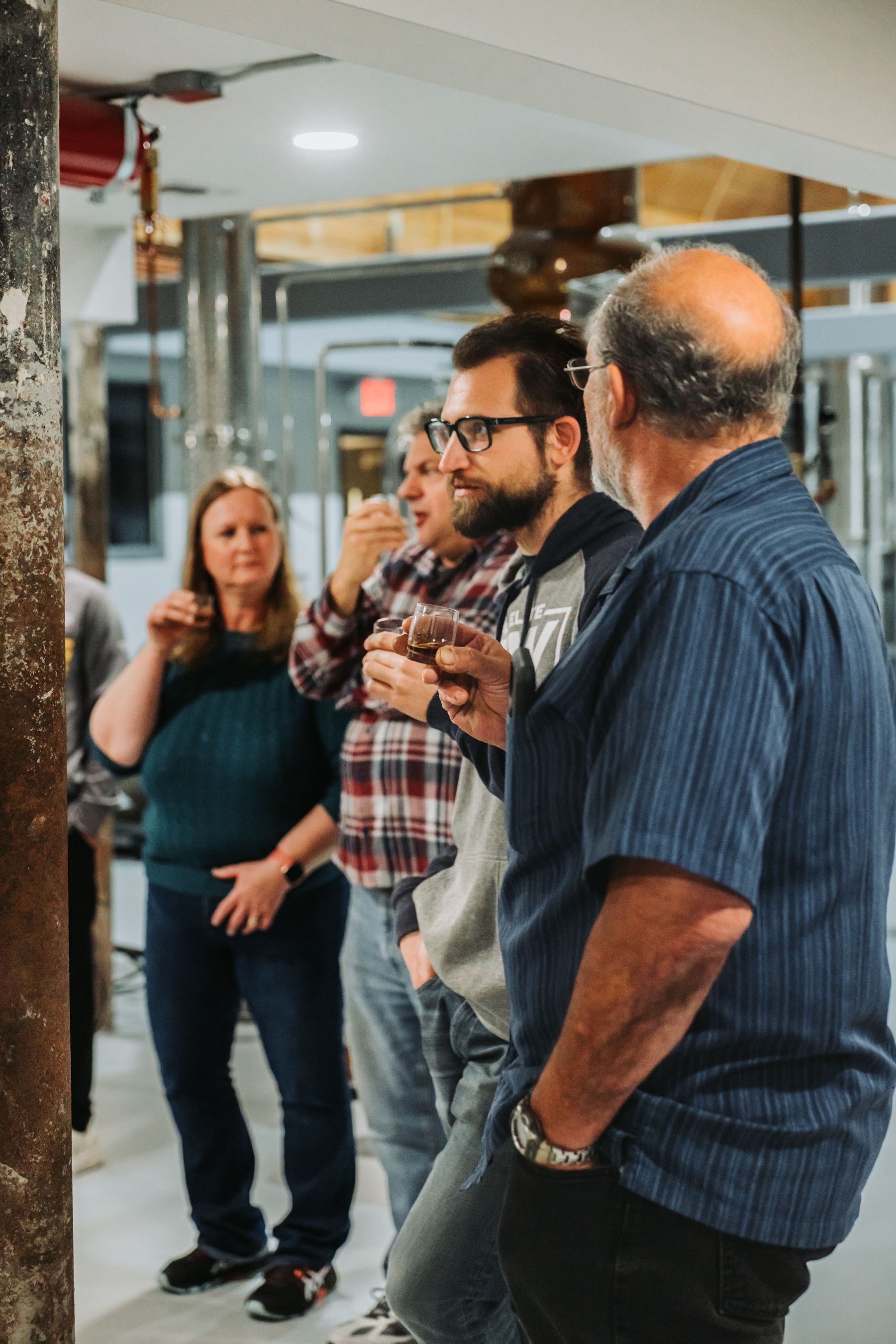 People gathered indoors, observing or discussing a small object. One man in blue shirt, others in casual clothing.