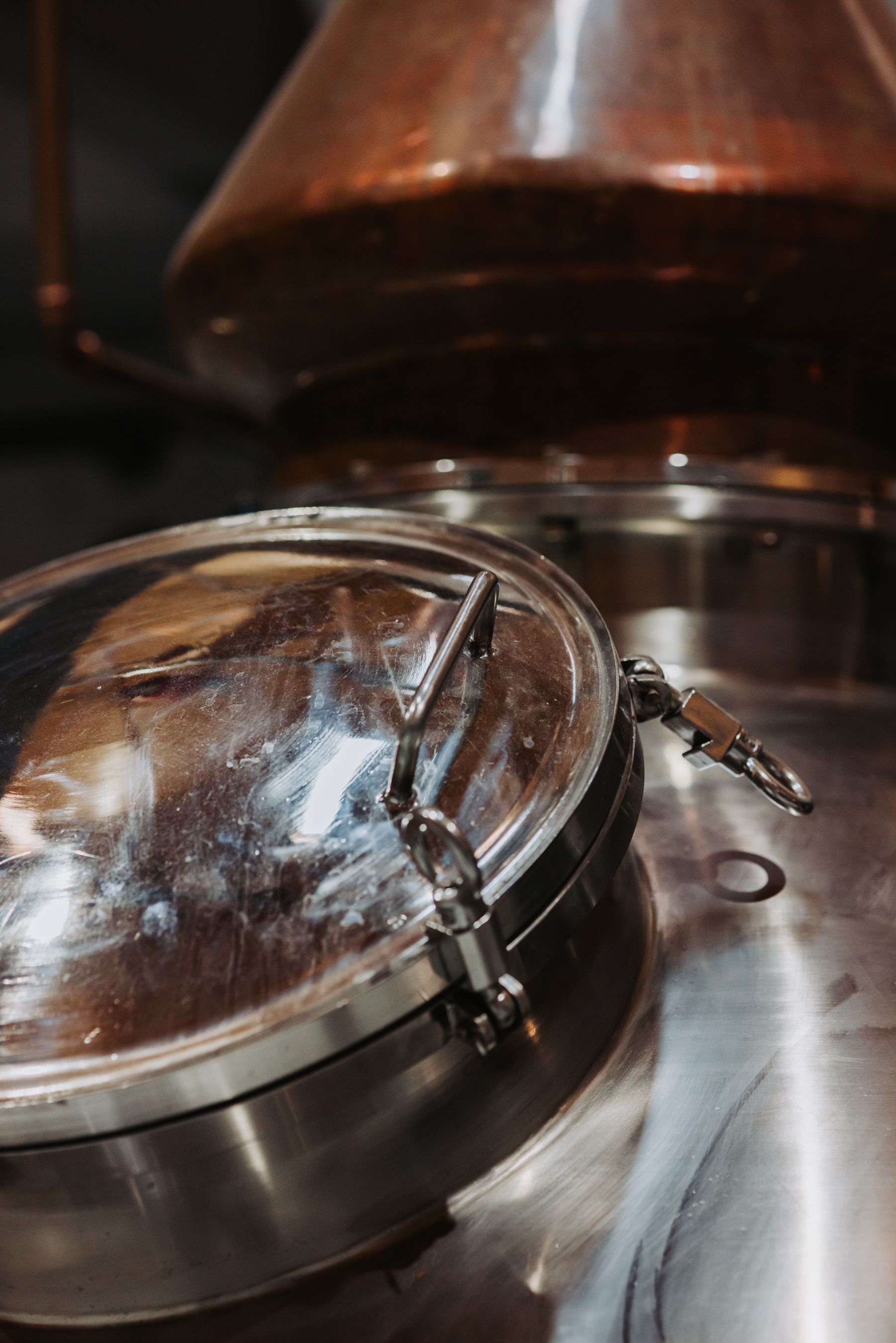 Close-up of a distillery tank lid, with copper top, in an industrial setting.