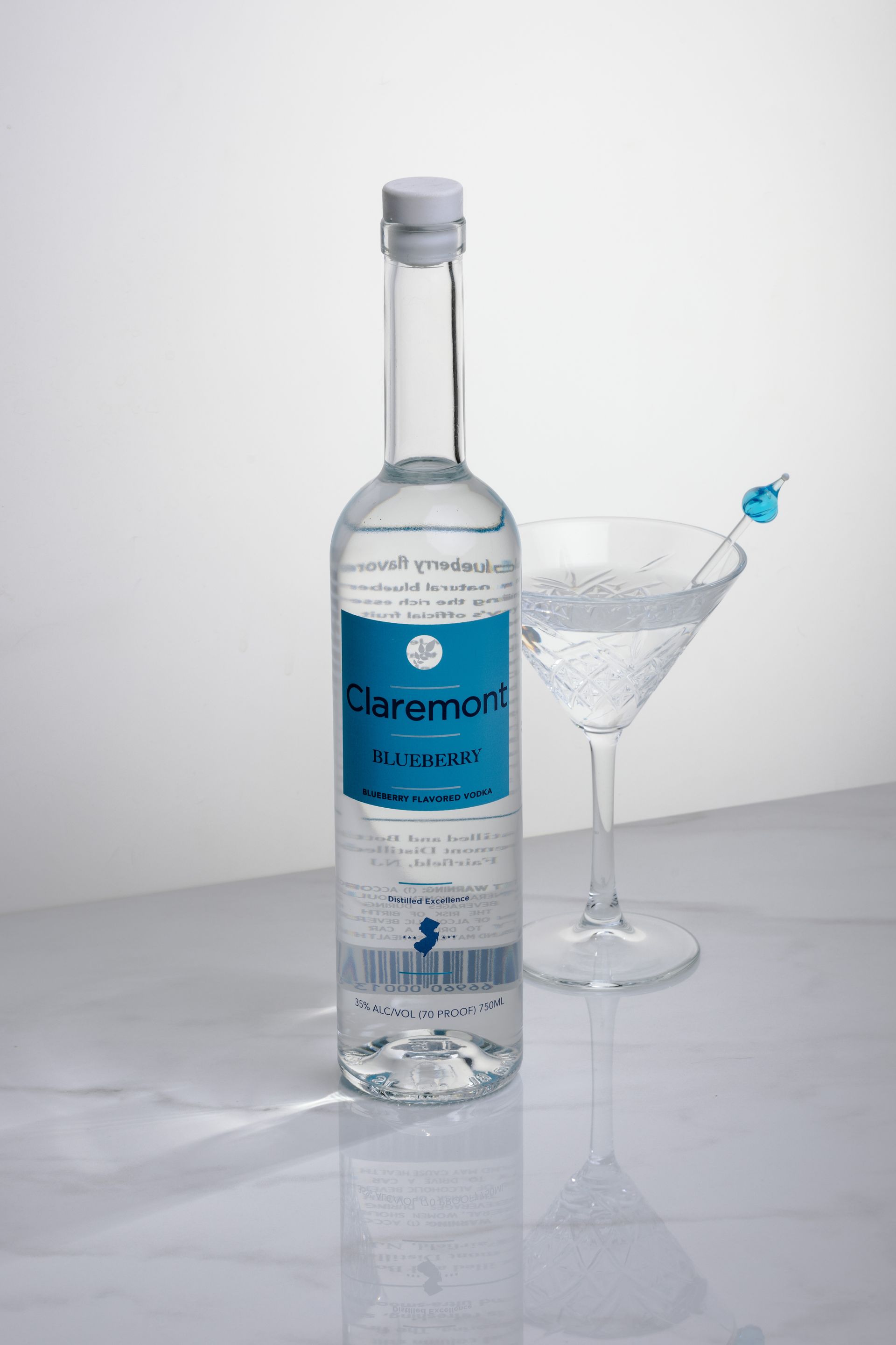 Bottle of Claremont Au Pinot with a filled martini glass on a marble surface, against a white backdrop.