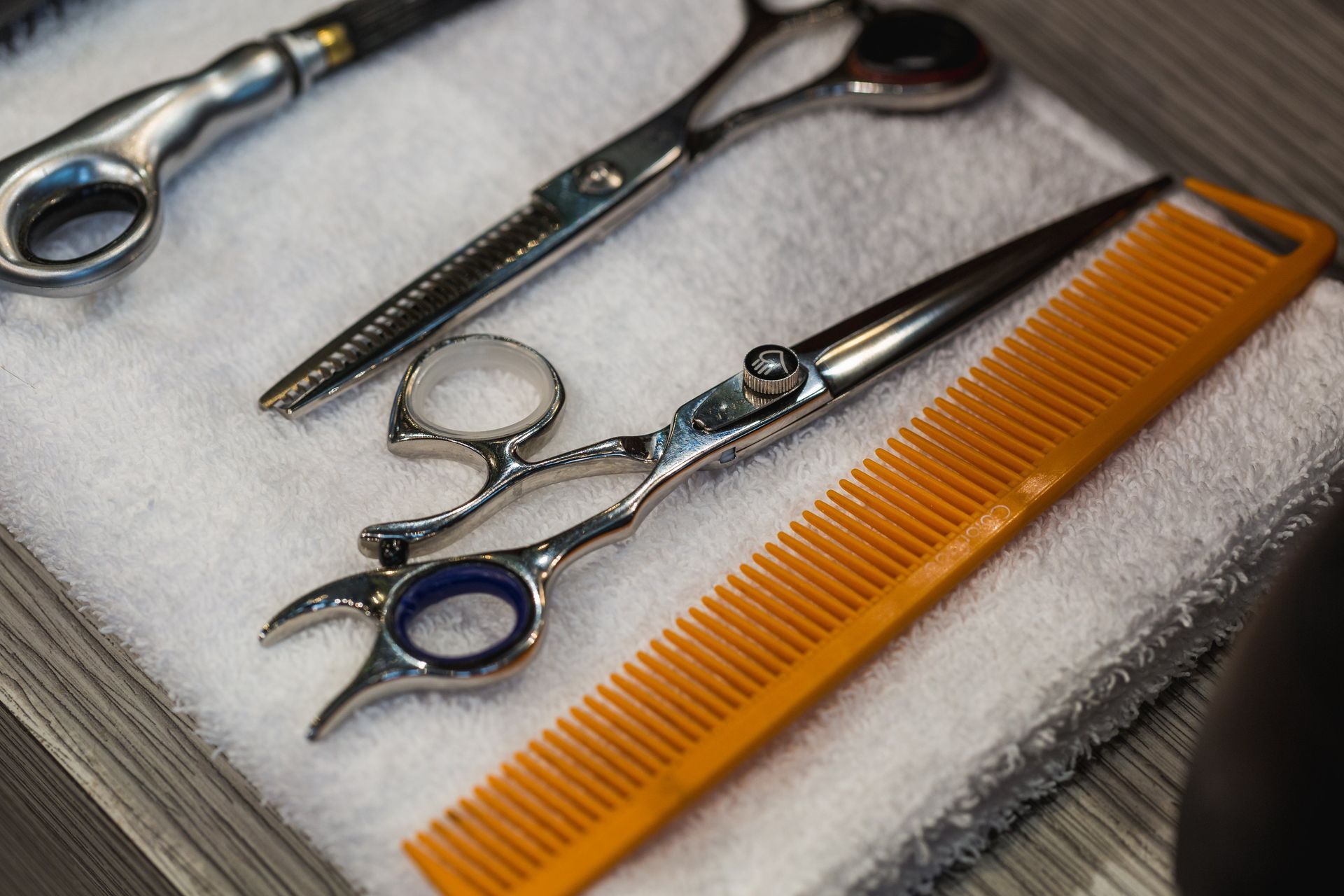 A comb, hair cutting shears, and thinning shears set atop of a white towel