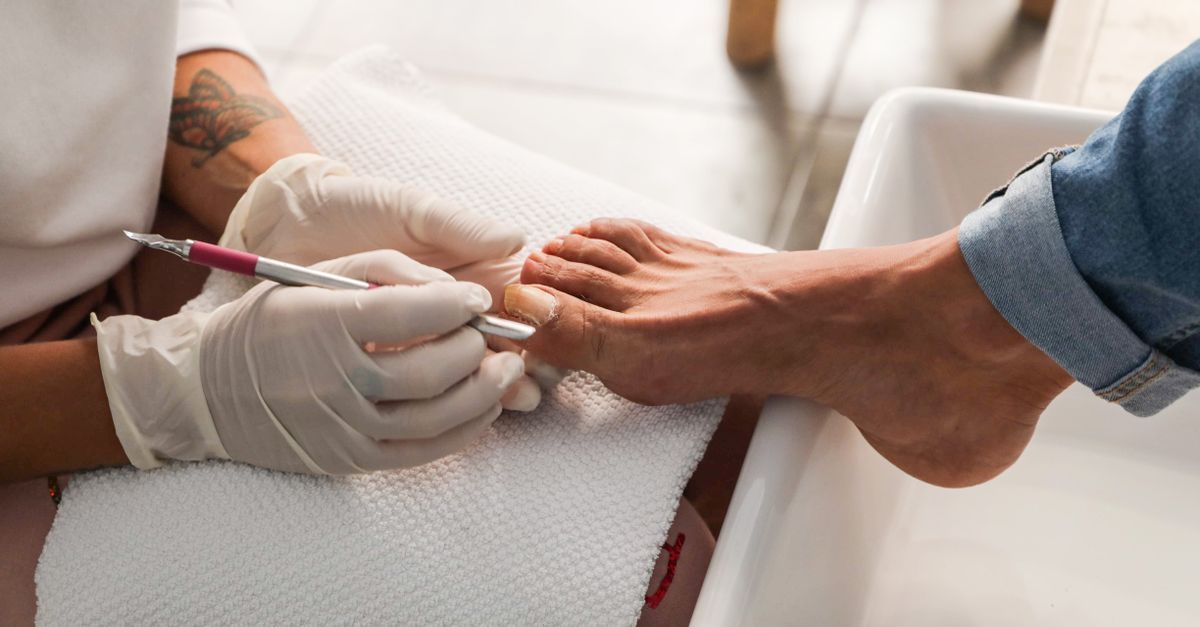 Pedicura en un salón, con guantes blancos, pintando las uñas de los pies de rojo