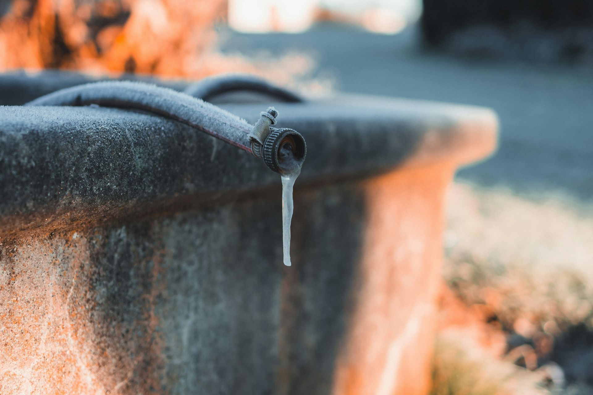 Frozen water dripping from a faucet on a concrete basin outdoors, with an orange-tinged background.