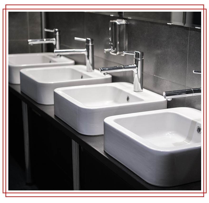 Four white rectangular sinks with chrome faucets in a modern bathroom.