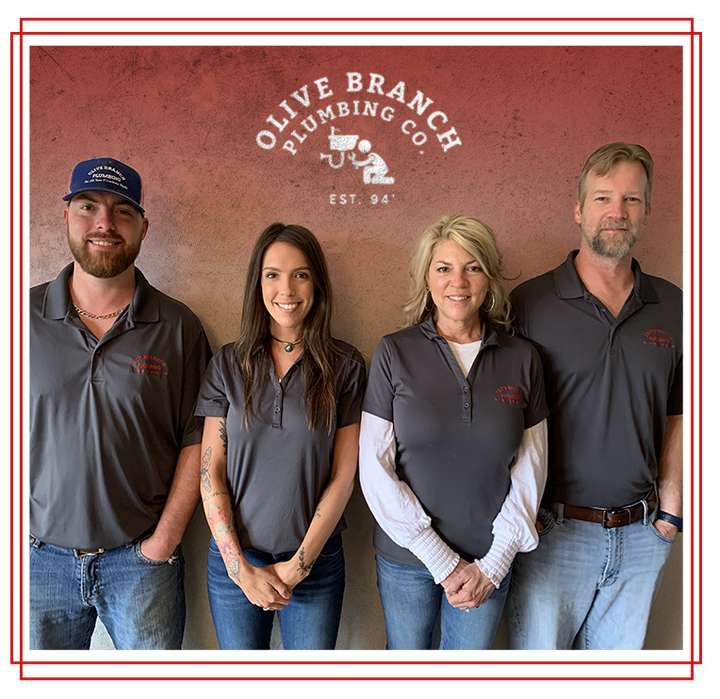 Four people of Olive Branch Plumbing, standing in front of a logo, wearing gray shirts and jeans.
