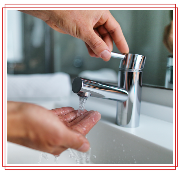 Person washes hands at a chrome faucet in a bathroom.