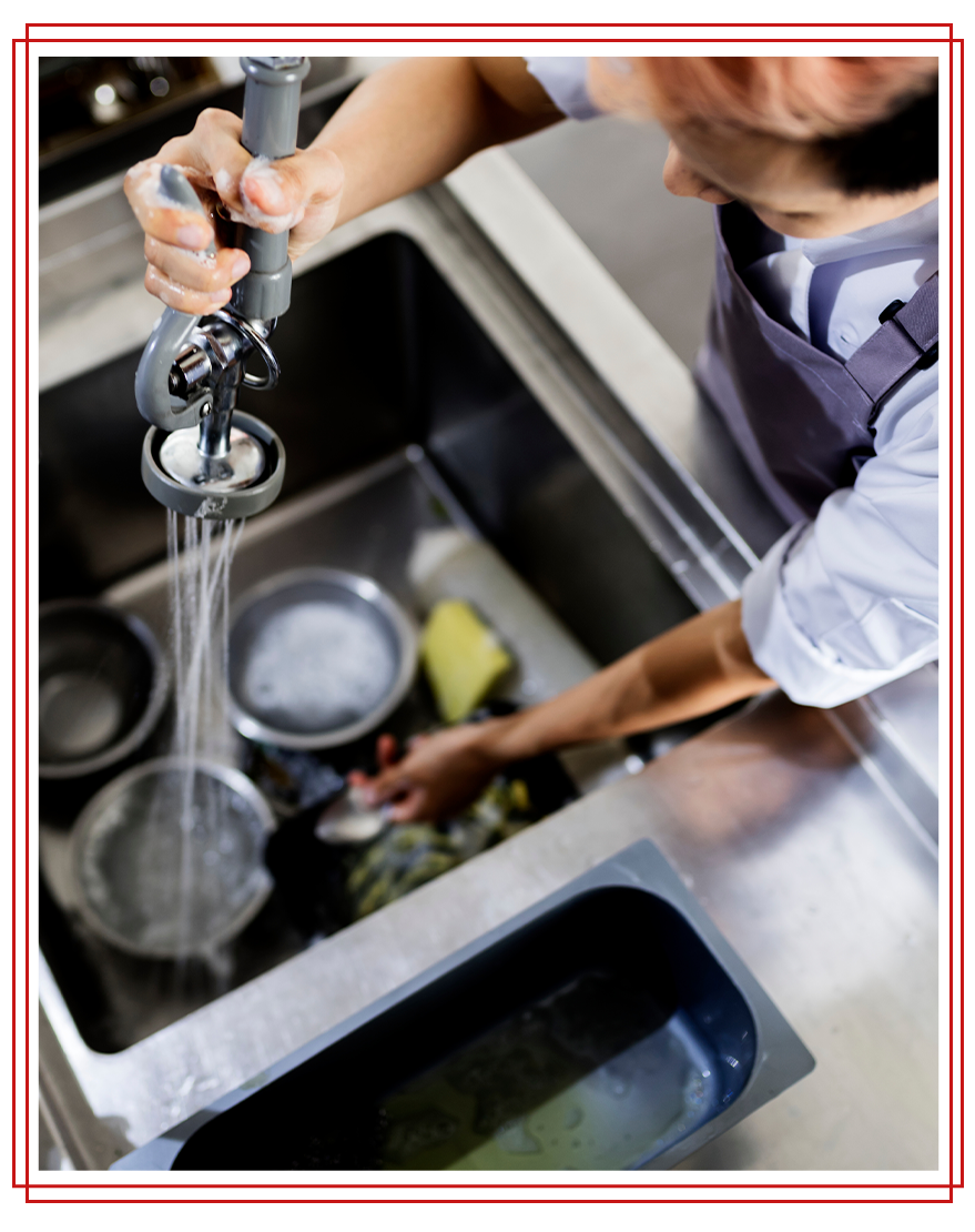 Person washing dishes in a stainless steel sink, using a sprayer.