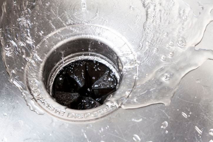 Water flowing down a stainless steel kitchen sink drain with a garbage disposal.