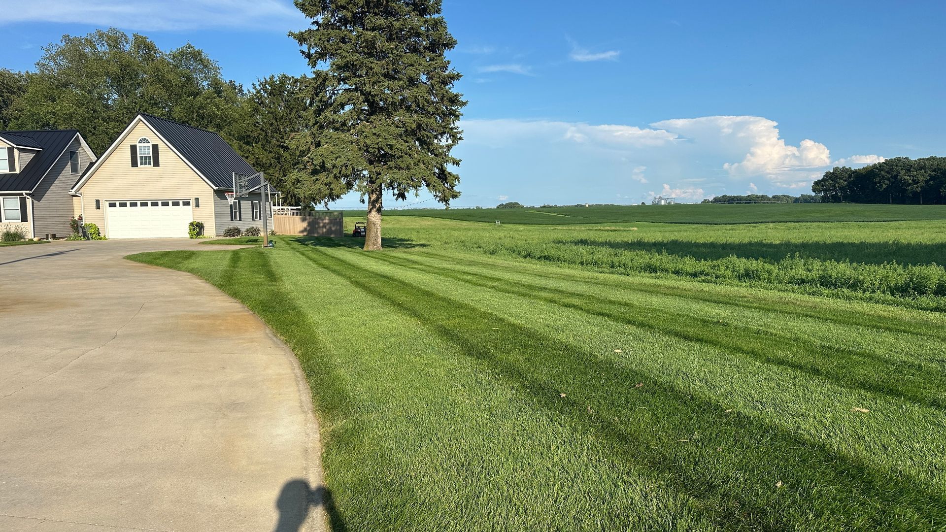 Suburban house beside a mowed green lawn and driveway under a clear blue sky