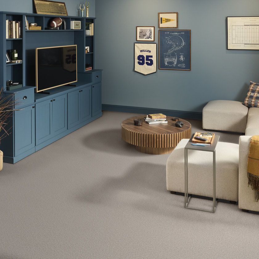 Blue living room with TV wall unit, beige sofa, round wood coffee table, and framed sports decor.