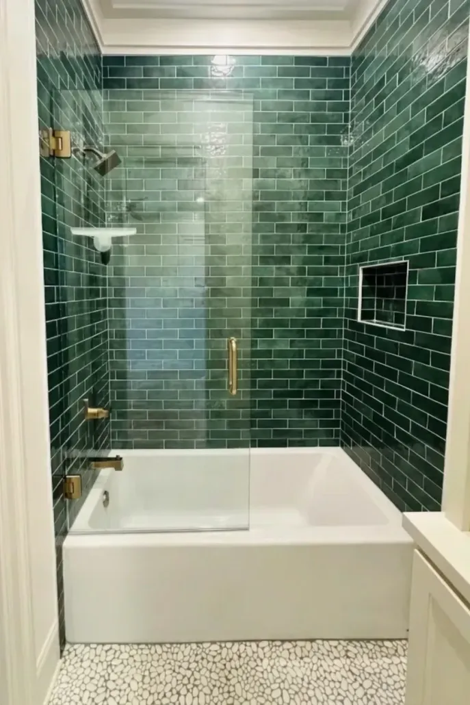 Green-tiled bathroom with a glass-enclosed bathtub shower and brass fixtures
