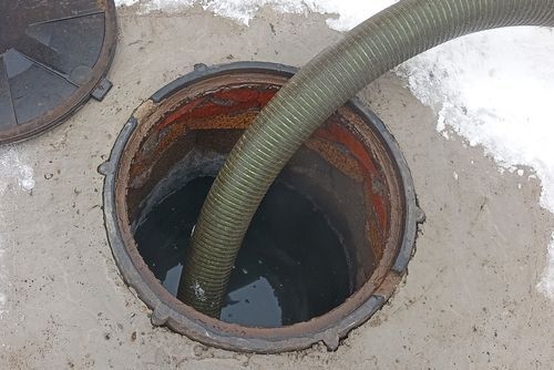 A hose pumps liquid waste from an open septic tank, set in concrete, with snow nearby.