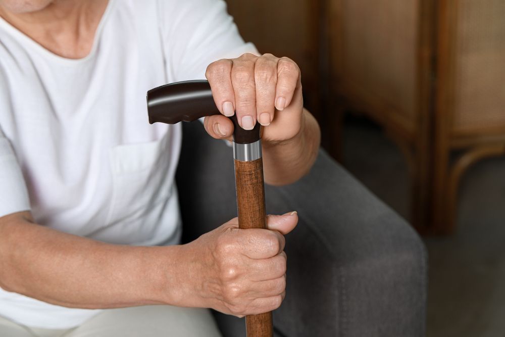 An elderly woman is sitting on a couch holding a cane.