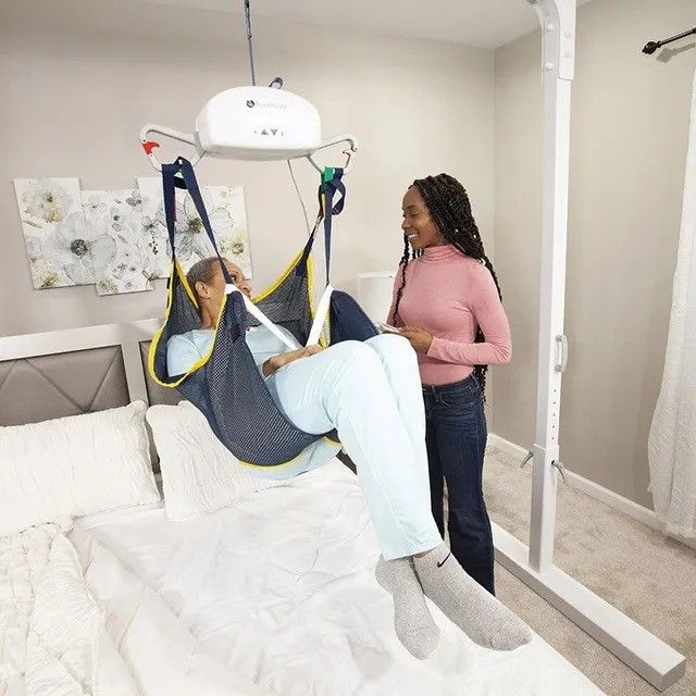 A woman is standing next to a woman in a sling on a bed