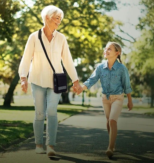 An elderly woman and a young girl are walking down a sidewalk holding hands.