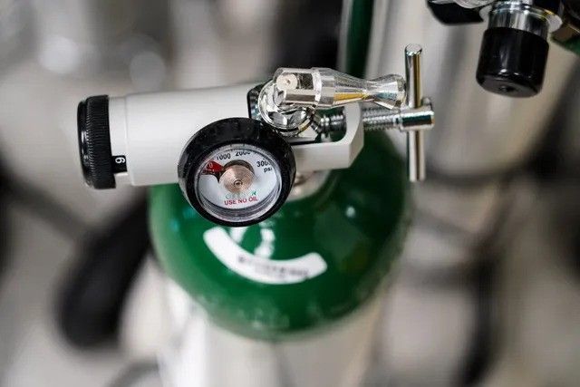A close up of an oxygen cylinder with a gauge attached to it.