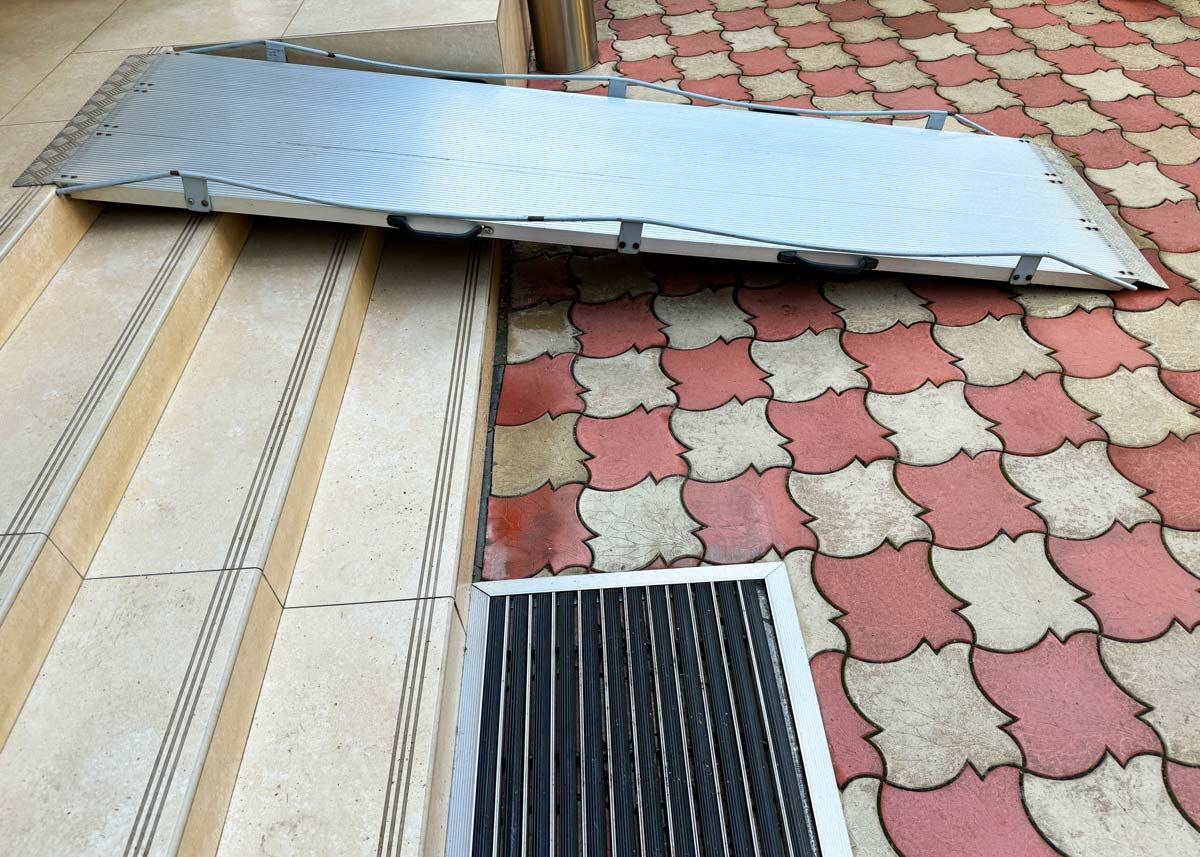 A portable handicap ramp is sitting on a brick floor next to stairs.