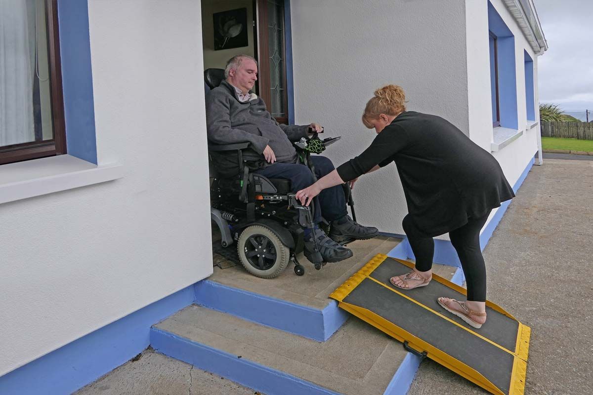 A woman is helping an elderly man on a portable wheelchair ramp for stairs.
