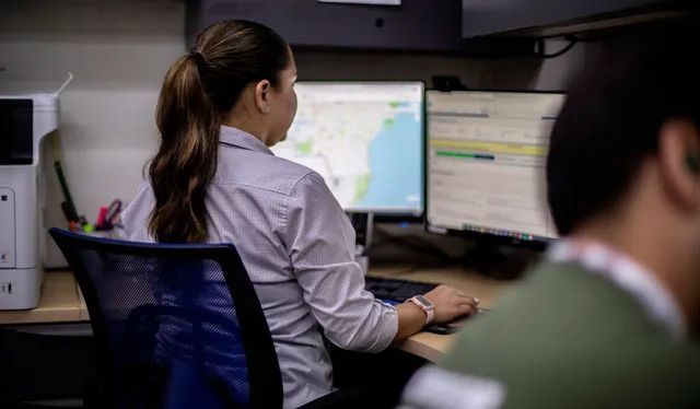 A woman is sitting at a desk in front of two computer monitors.