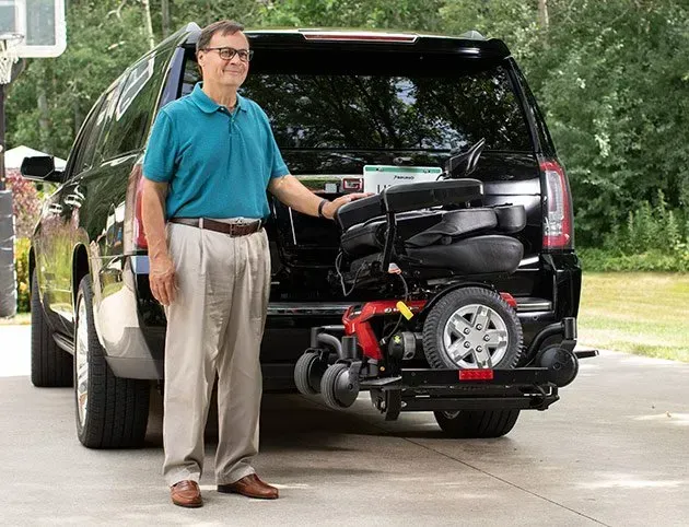 A man is standing in front of a truck with a mobility scooter in the back.