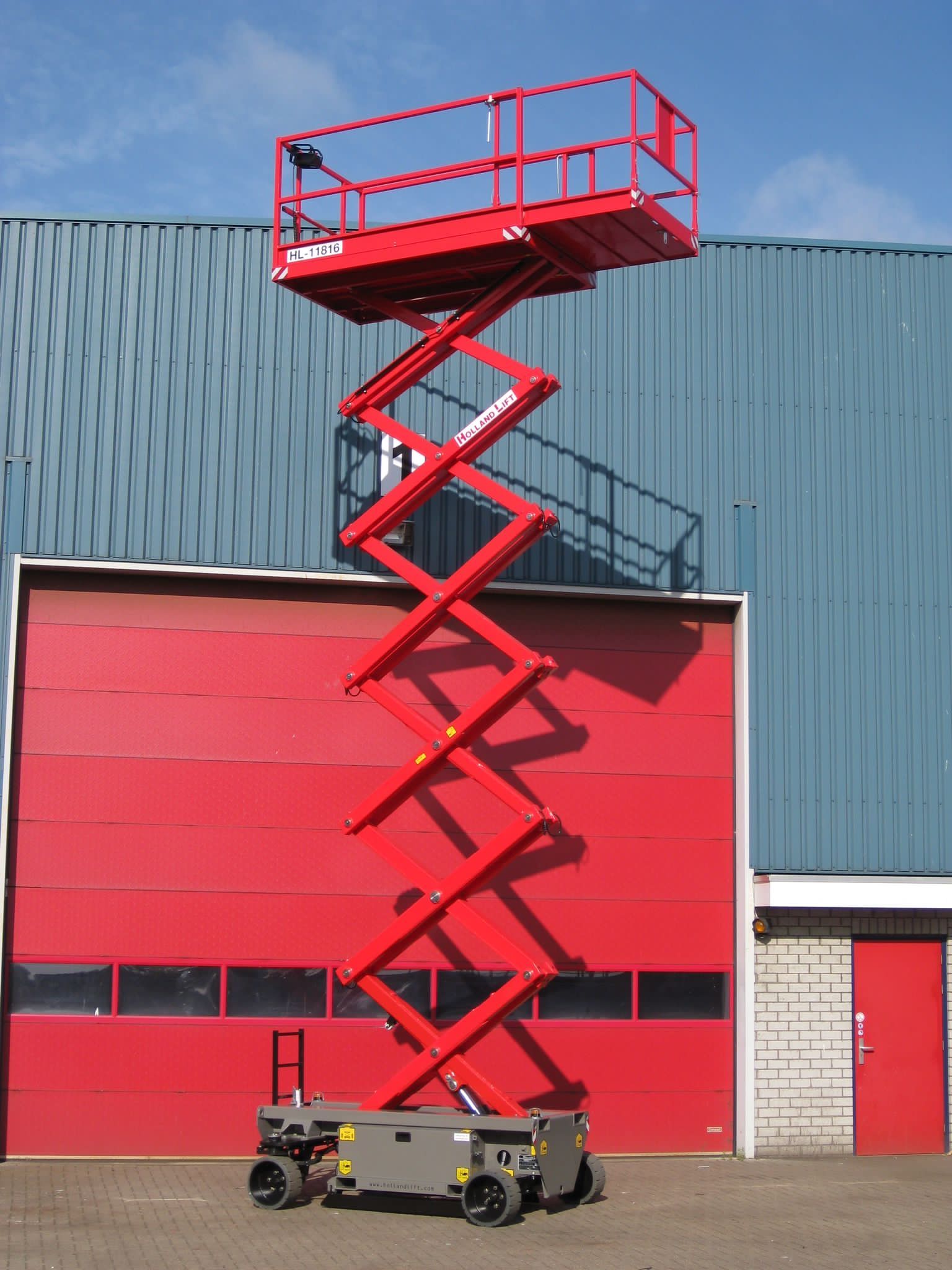 Red scissor lift raised in front of a red door and blue building.