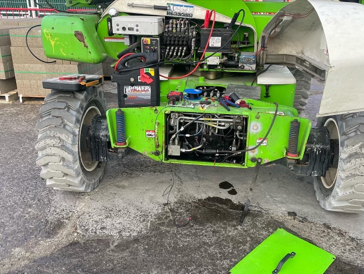 Green industrial machinery being serviced outdoors; parts exposed.