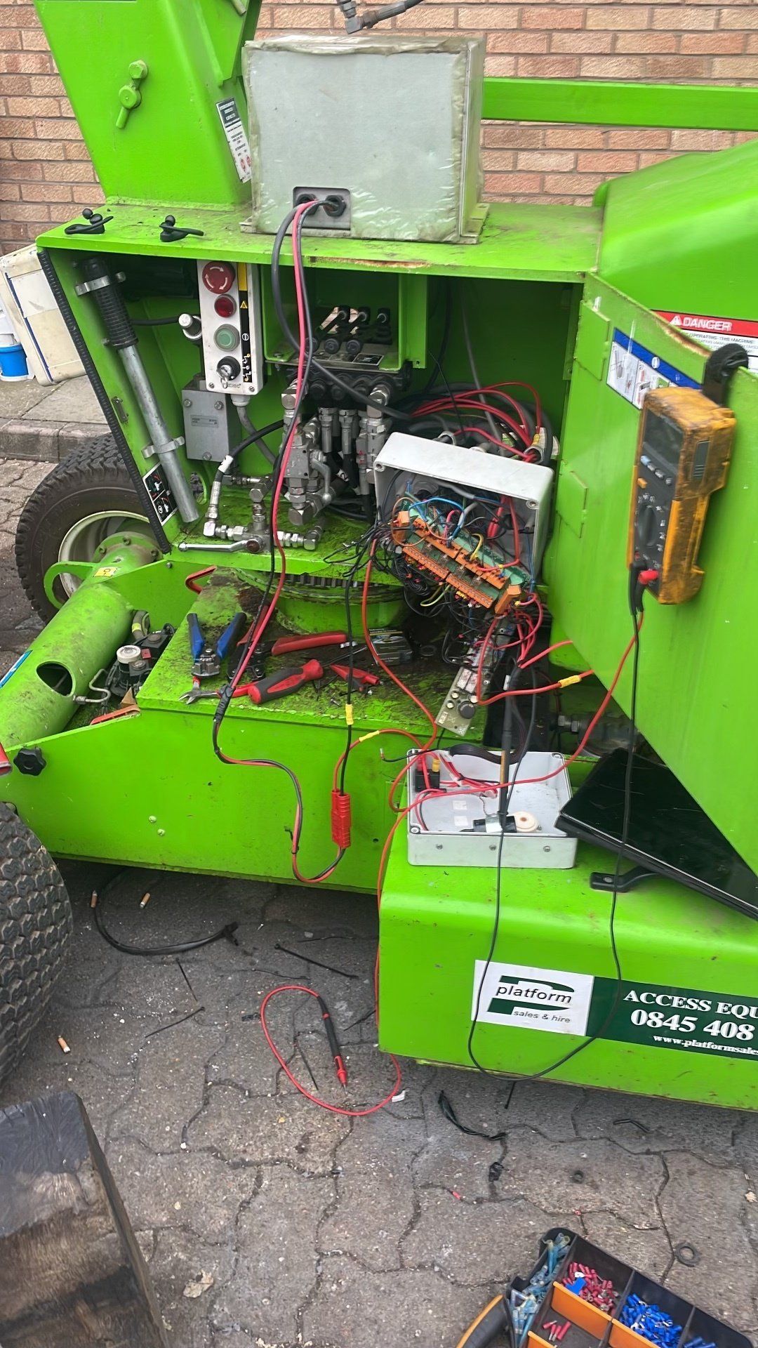 Green wood chipper open, wires exposed, with multimeter testing electrical components.