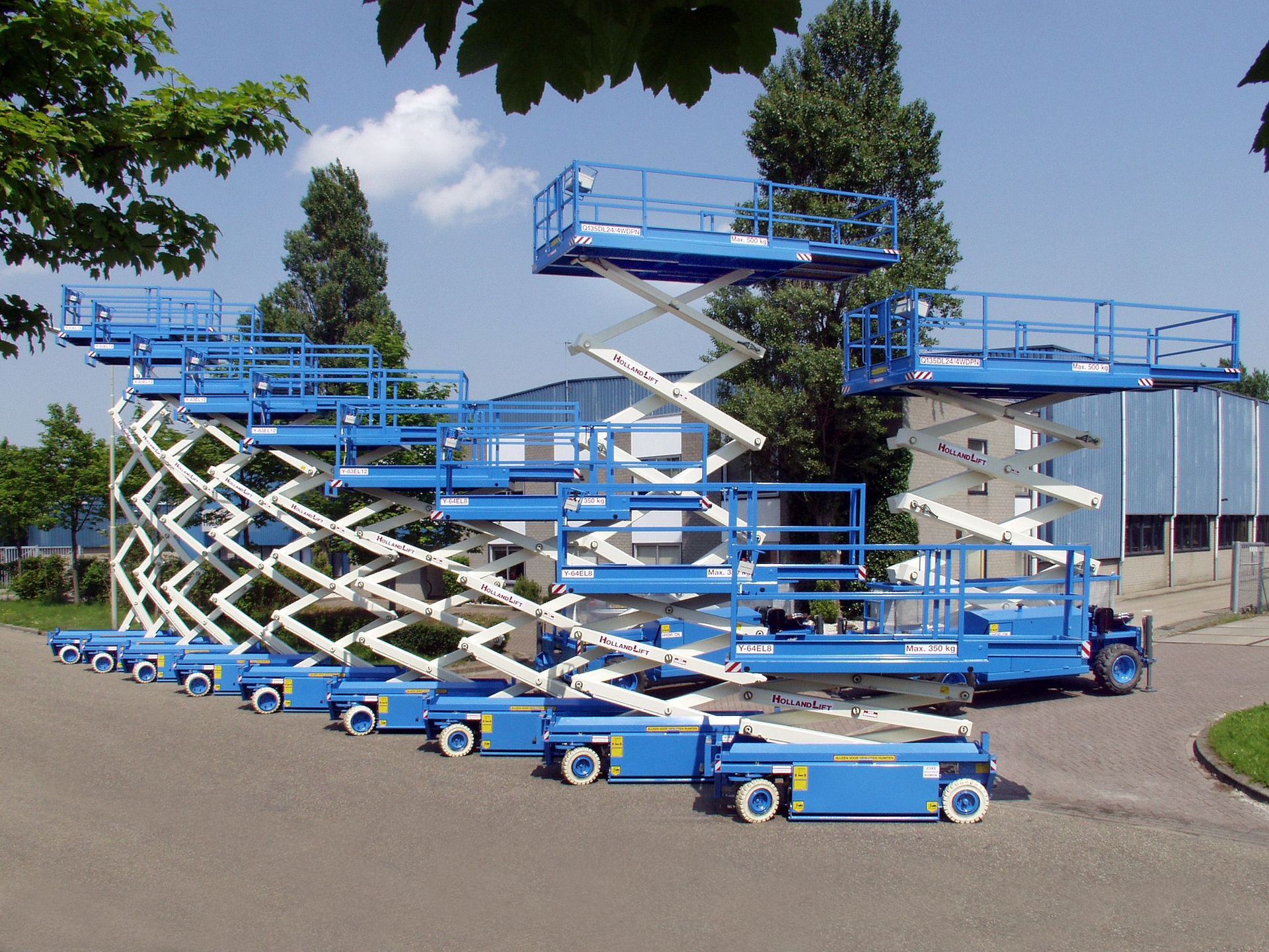 Blue scissor lifts stacked, reaching upwards. Outdoors, on a road.