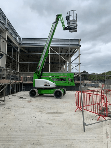 Green aerial work platform next to a building under construction, extending upwards.