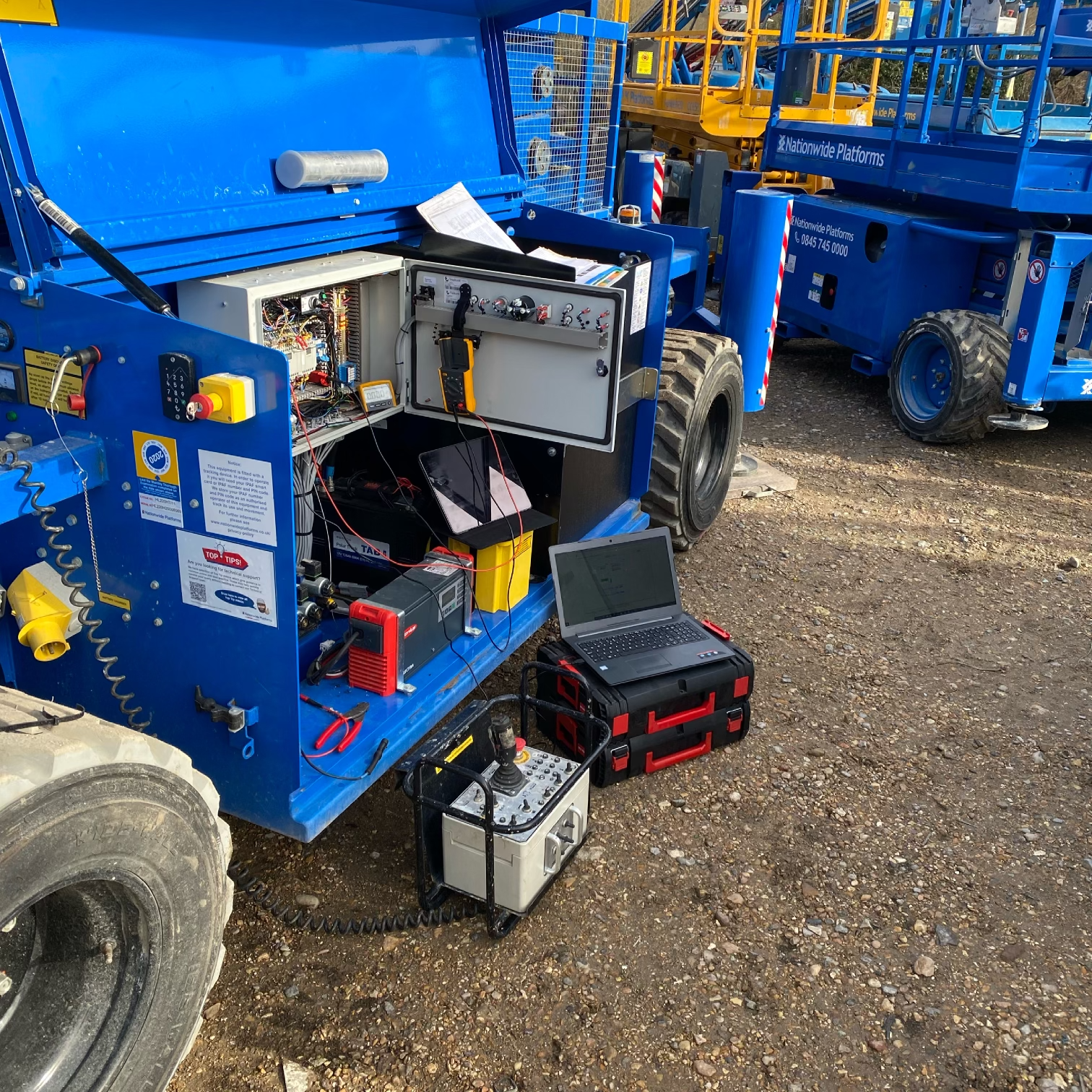 Blue aerial lift with open electrical panel, laptop, and diagnostic equipment outdoors.