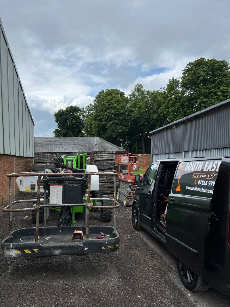 Green lift platform and black van parked next to buildings, cloudy sky overhead.