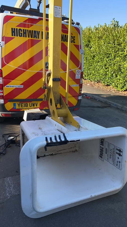 A white debris collector on a yellow hydraulic lift attached to a highway maintenance van with chevron stripes.