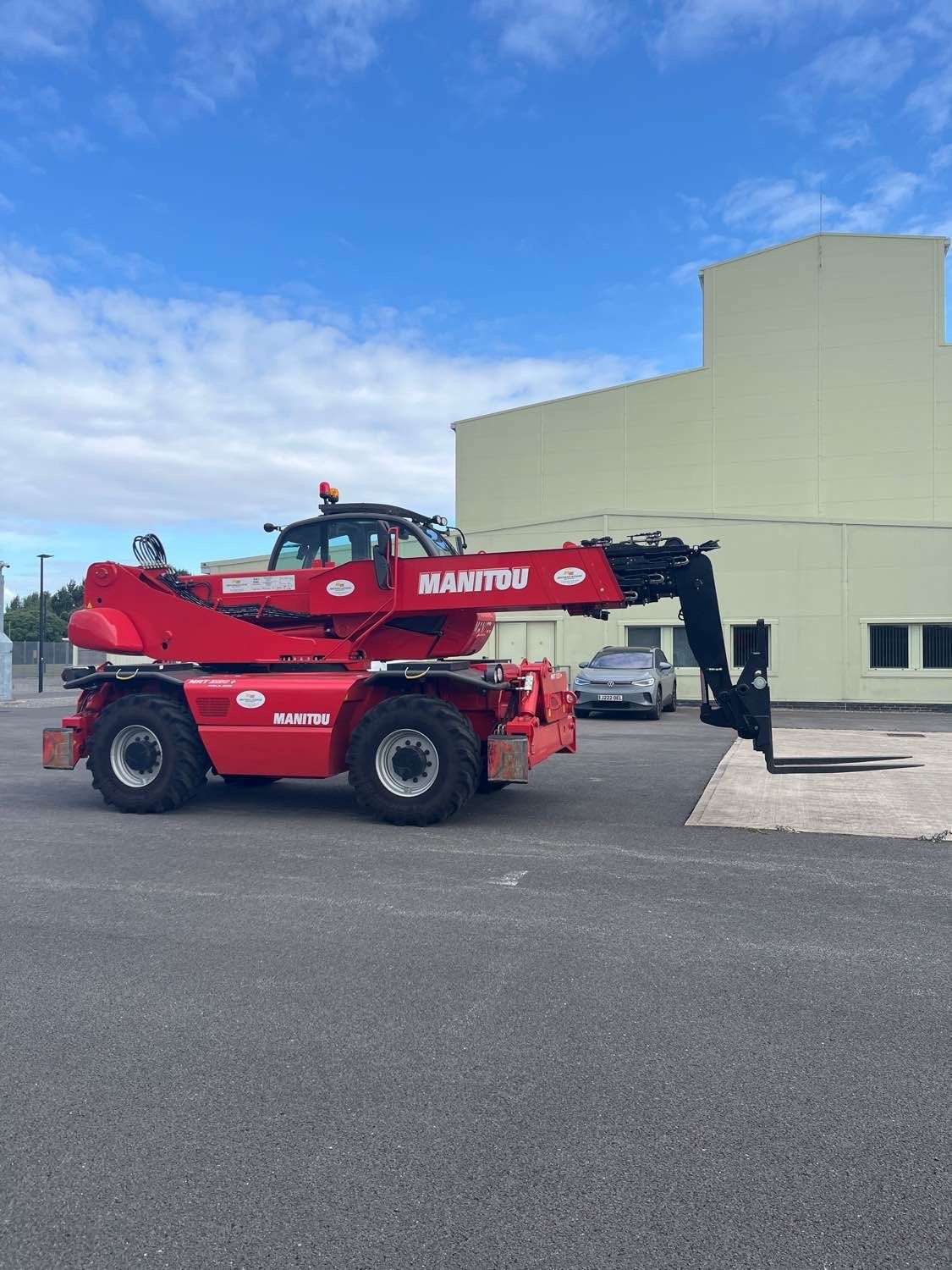 Red Manitou telehandler on asphalt next to a light green building.