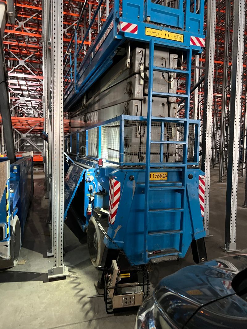 Blue scissor lift in a warehouse, near metal shelving.
