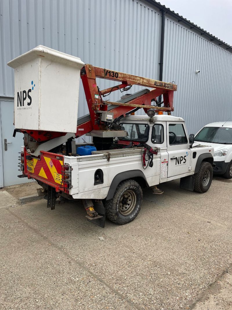 White utility truck with aerial lift in front of a building; it has NPS logo and warning signs.