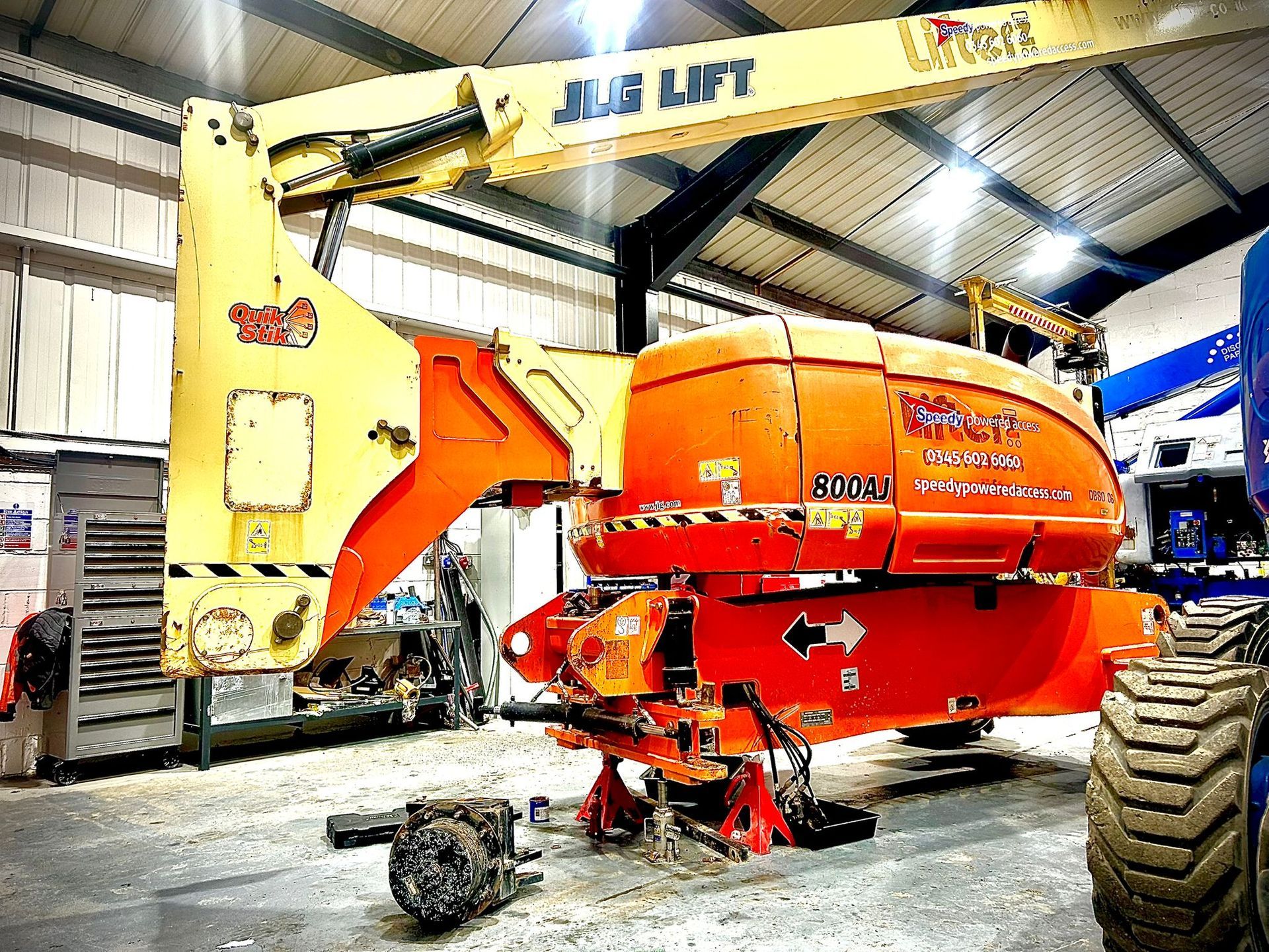A large, orange and yellow JLG lift machine in a workshop, under repair.